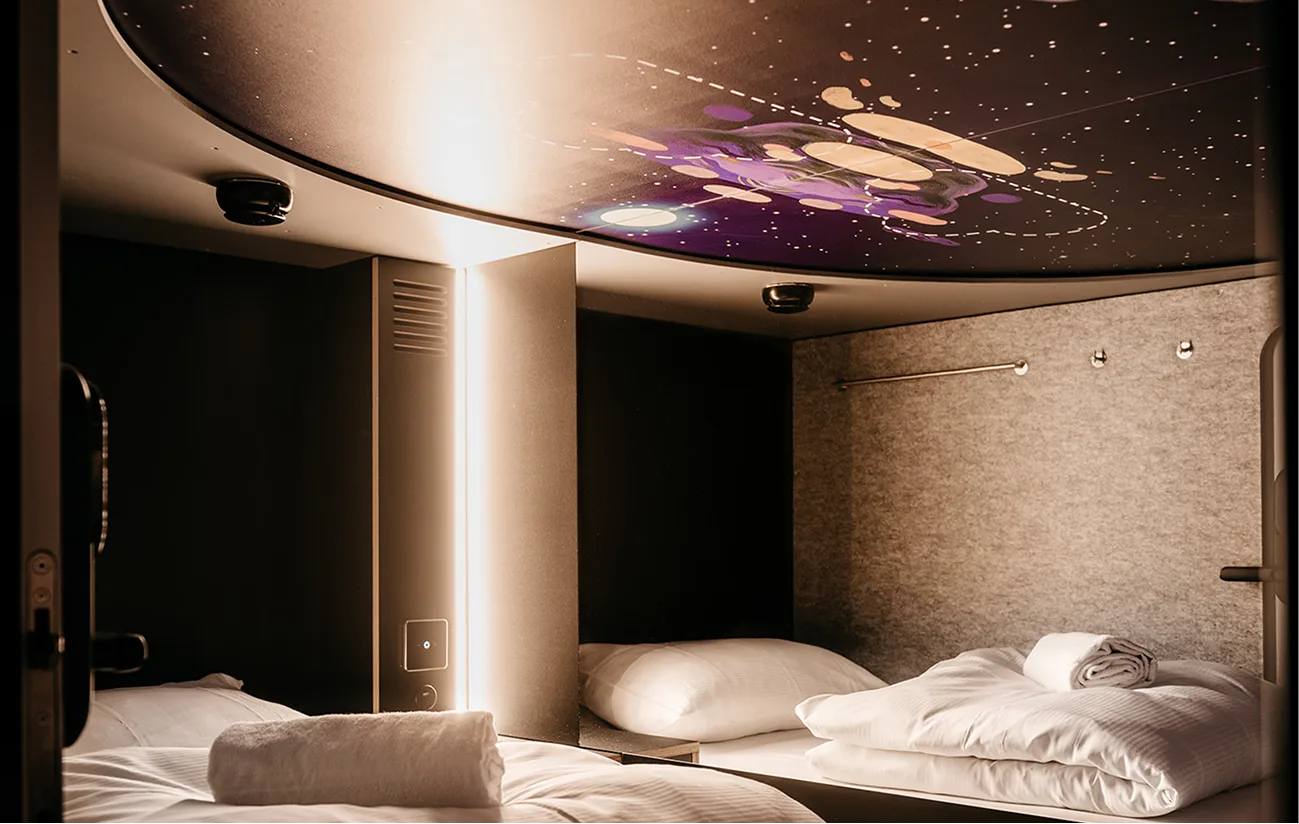 Capsule Hotel modern twin sleeping pods with warm lighting, galaxy ceiling art, white bedding and rolled towels
