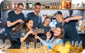 Capsule Hotel team celebrating behind the bar, cheering and pointing to an award, with beers and wine glasses.