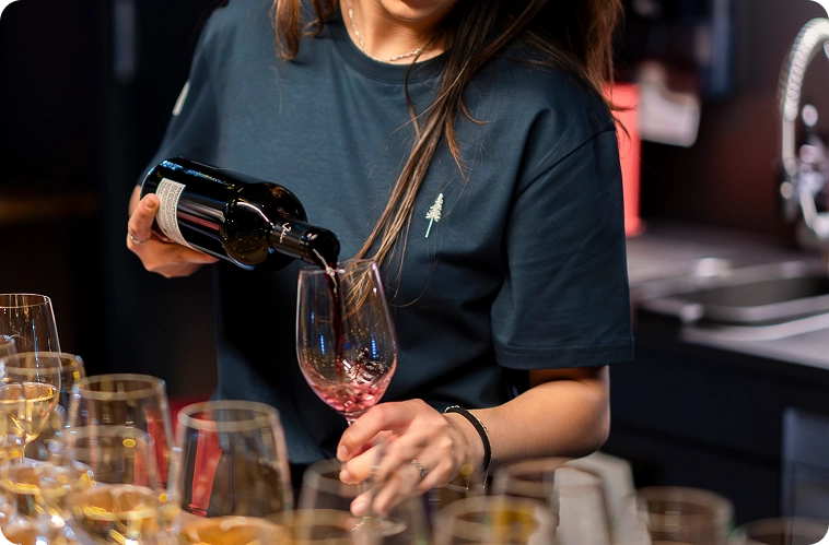 Capsule Hotel staff member pouring red wine into a glass at the bar, with rows of stemware on the counter.