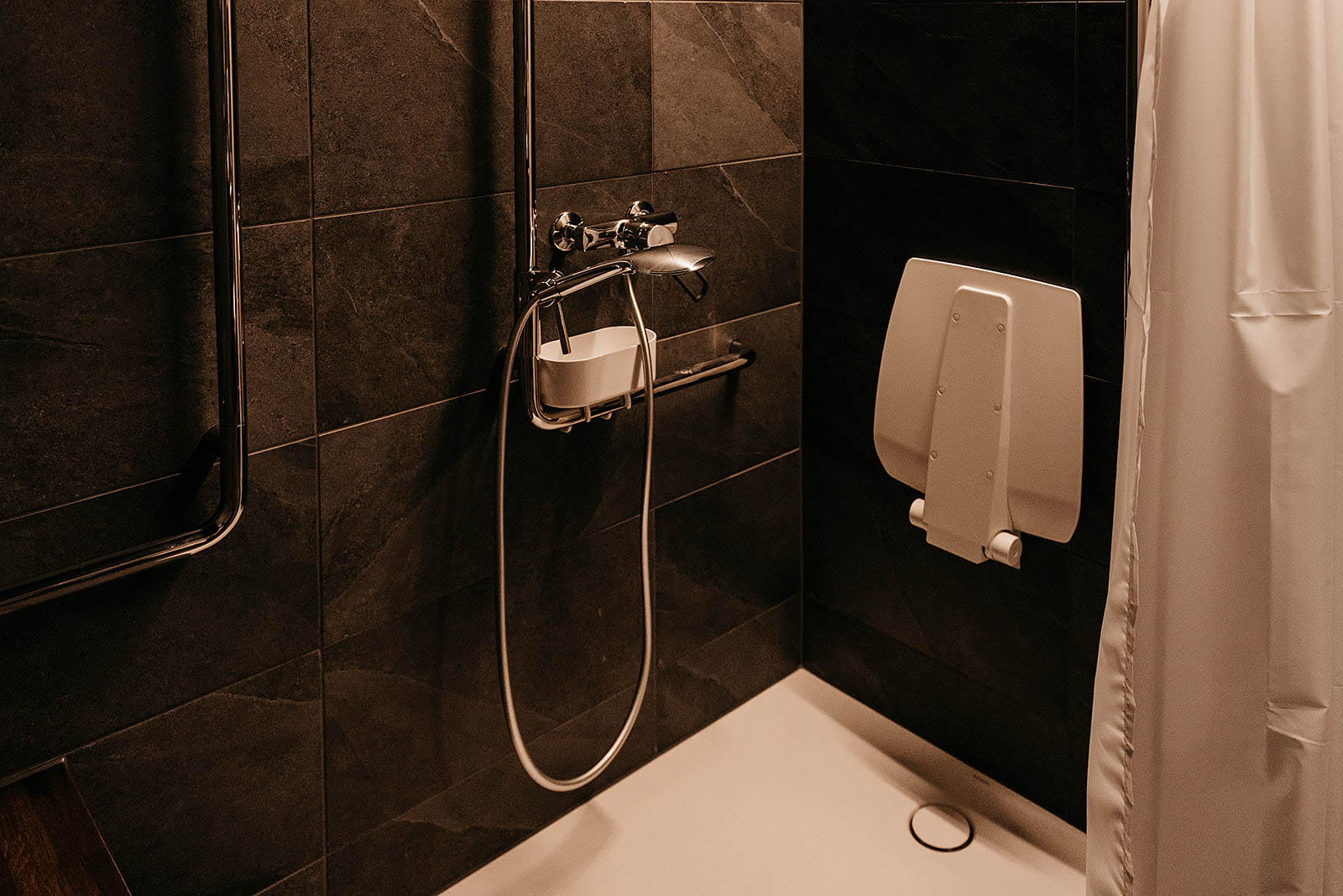 Shower area with dark tiles and a white curtain at Capsule Hotel Lucerne Old Town.