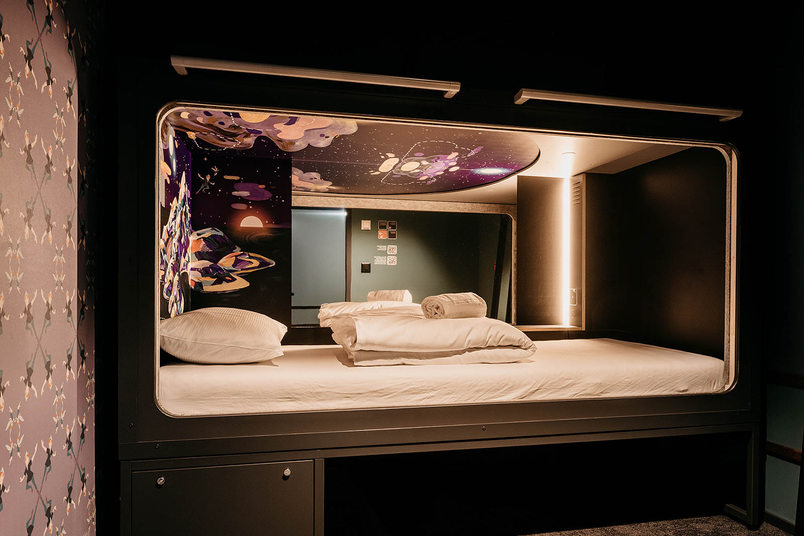 Brightly lit capsule room with space-themed decor at Capsule Hotel Lucerne Old Town.