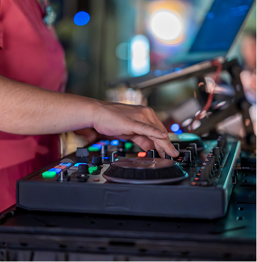 Hands mixing on a DJ controller at Capsule Hotel lounge, with laptop and colorful lights in the background.