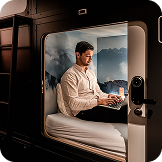 Guest working on a laptop in a modern capsule with mountain mural at Capsule Hotel.