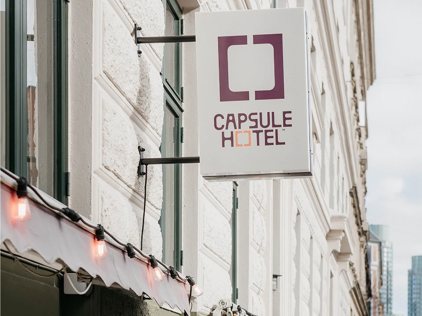 Capsule Hotel exterior sign with purple square logo on a historic European street facade