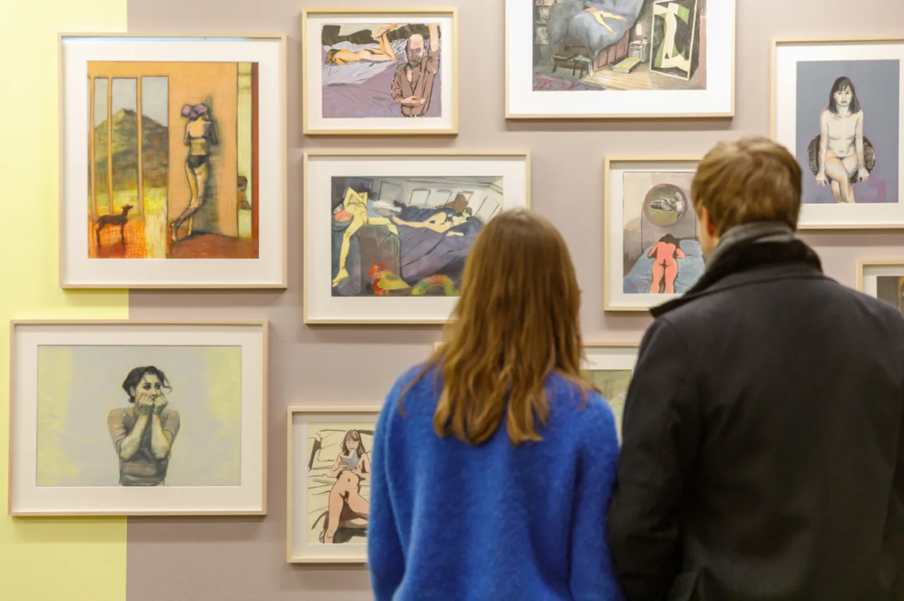 Zwei Besucher betrachten eine Wand mit gerahmten figurativen Zeichnungen im Cartoonmuseum Basel