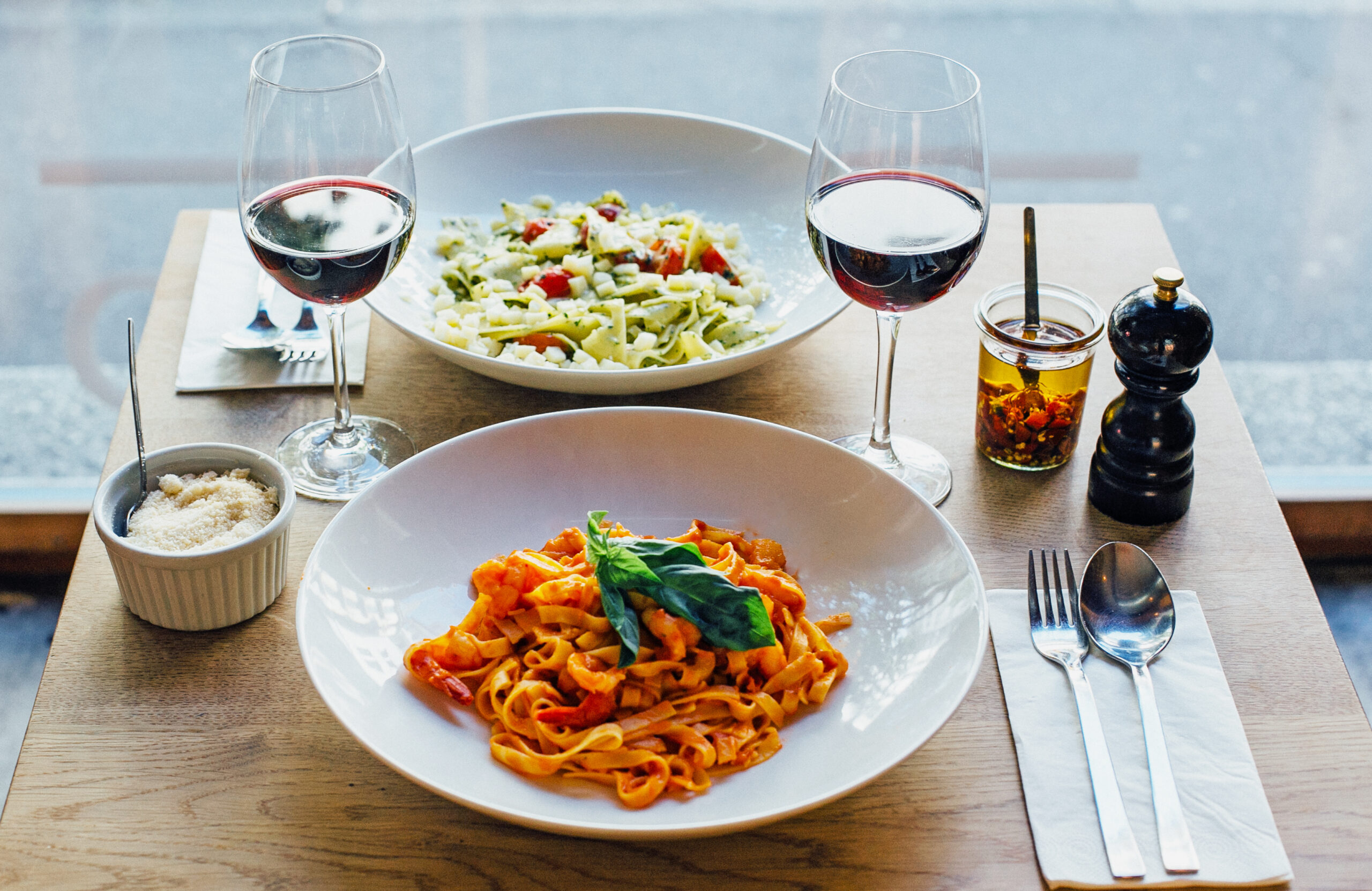 Pasta und Salat im Capsule Hotel mit Rotwein, Basilikum-Tagliatelle, Parmesan, Chiliöl und Pfeffer auf einem Holztisch.