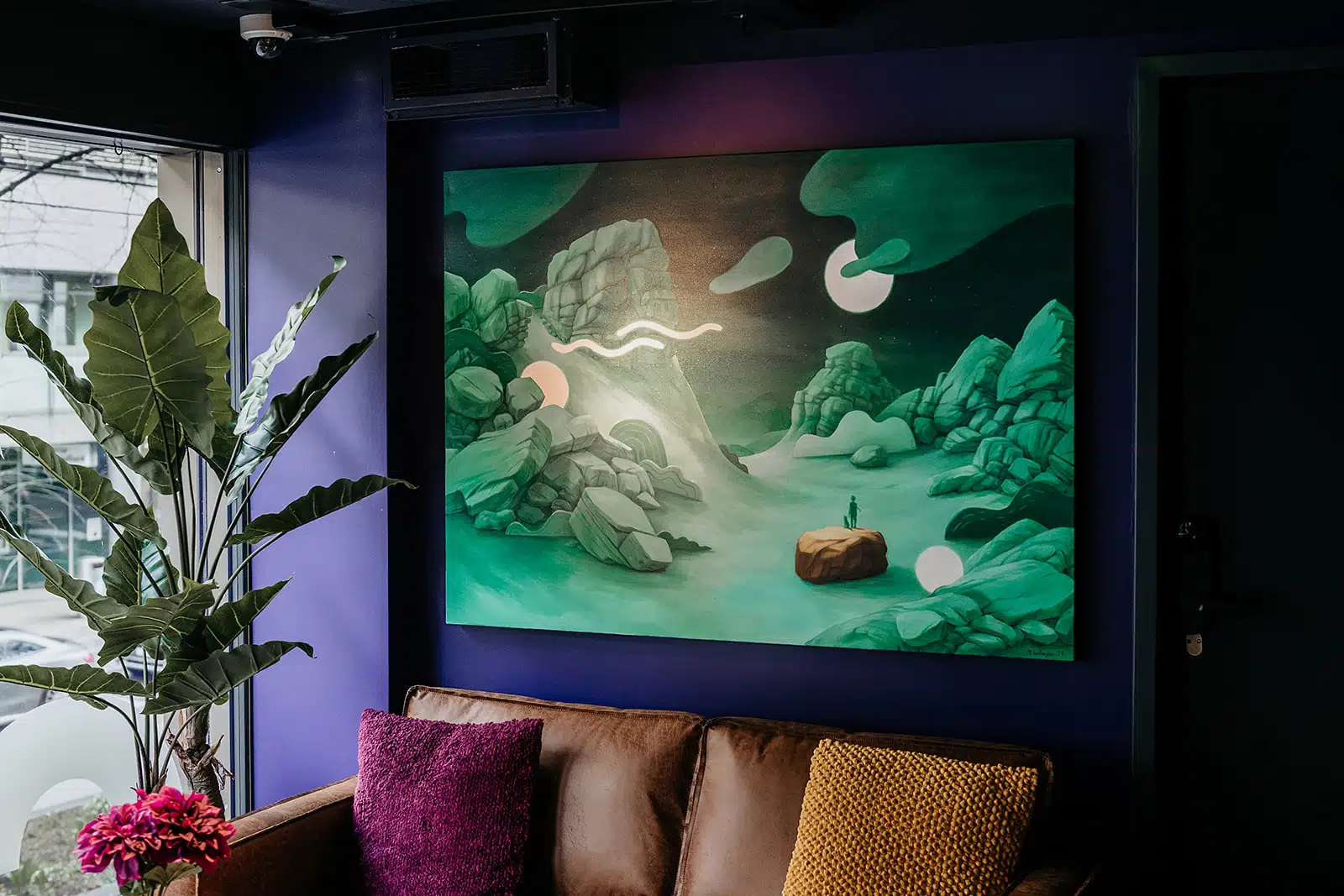 Cozy Capsule Hotel common area with a contemporary landscape painting, vibrant pillows, and a potted plant.