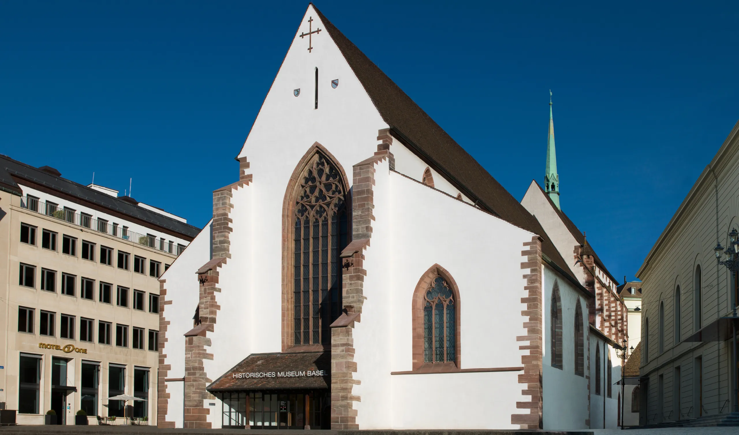 Die weiße gotische Fassade der Barfüsserkirche, Sitz des Historischen Museums Basel, unter strahlend blauem Himmel