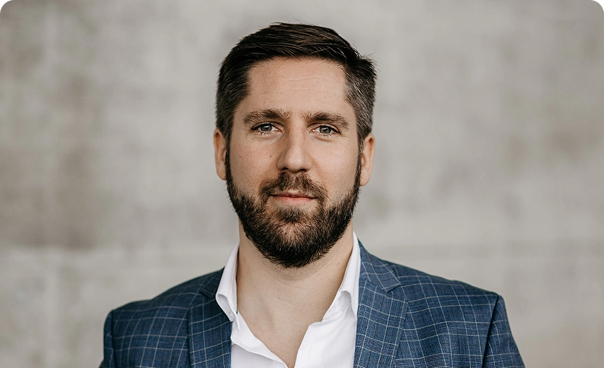 Capsule Hotel team portrait: bearded man in blue checked blazer against neutral concrete background
