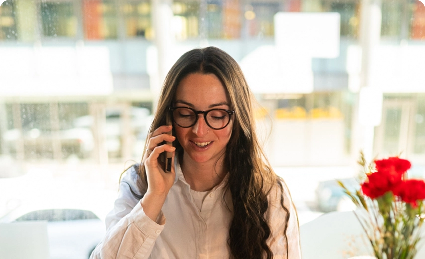 Smiling team member with long dark hair and glasses on a call at Capsule Hotel, warm ambiance in the background.