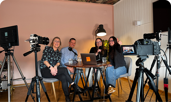Group podcast recording at Capsule Hotel with three women and a man seated around a table in a cozy setting.