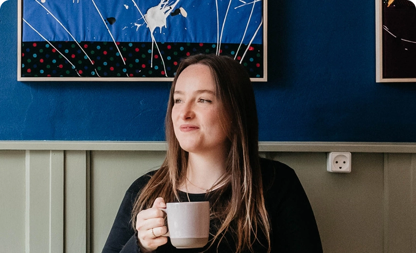 Young woman enjoying a coffee at Capsule Hotel, vibrant blue art on wall, creating a cozy ambiance.