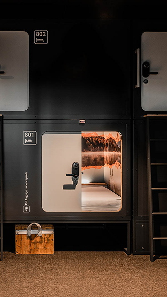 Open sleeping pod 801 with mountain mural and crisp bedding at Capsule Hotel, stacked capsule units with ladder.