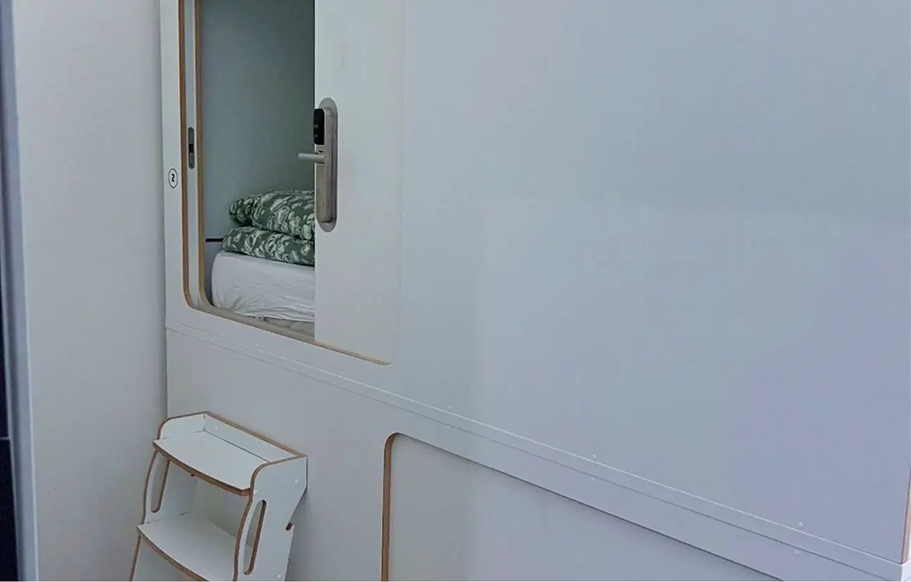 Cozy sleeping pod with bed and floral bedding at Capsule Hotel, featuring modern design and privacy.