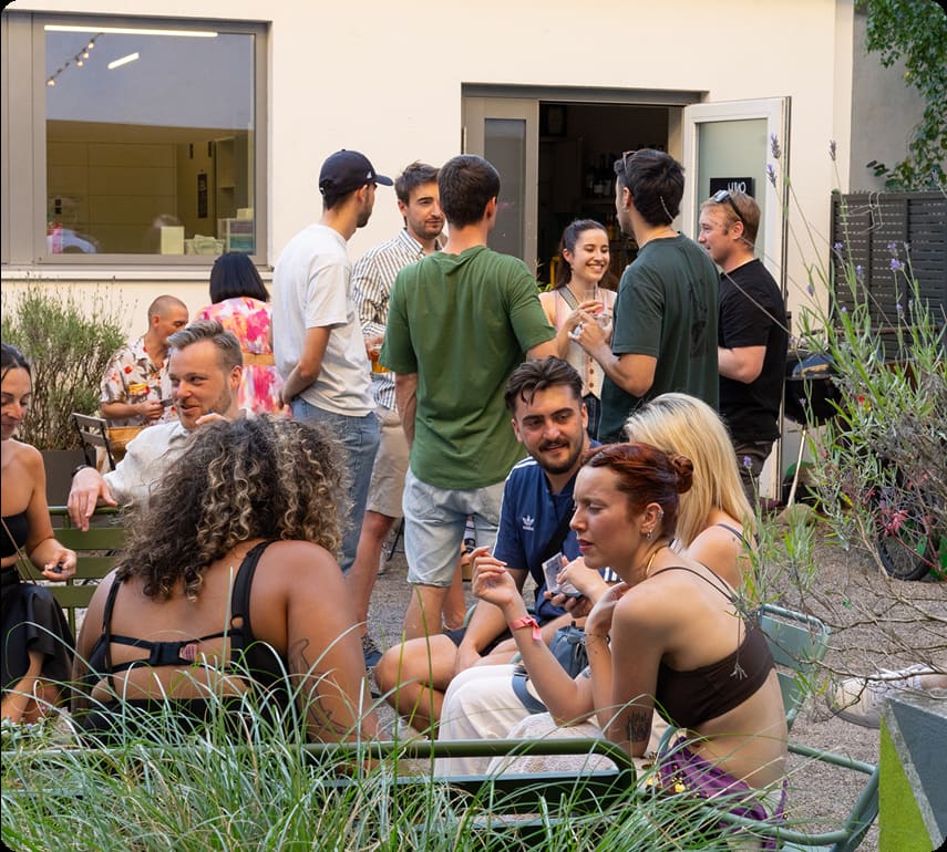 Guests socializing in Capsule Hotel courtyard garden, chatting over drinks on a sunny afternoon.
