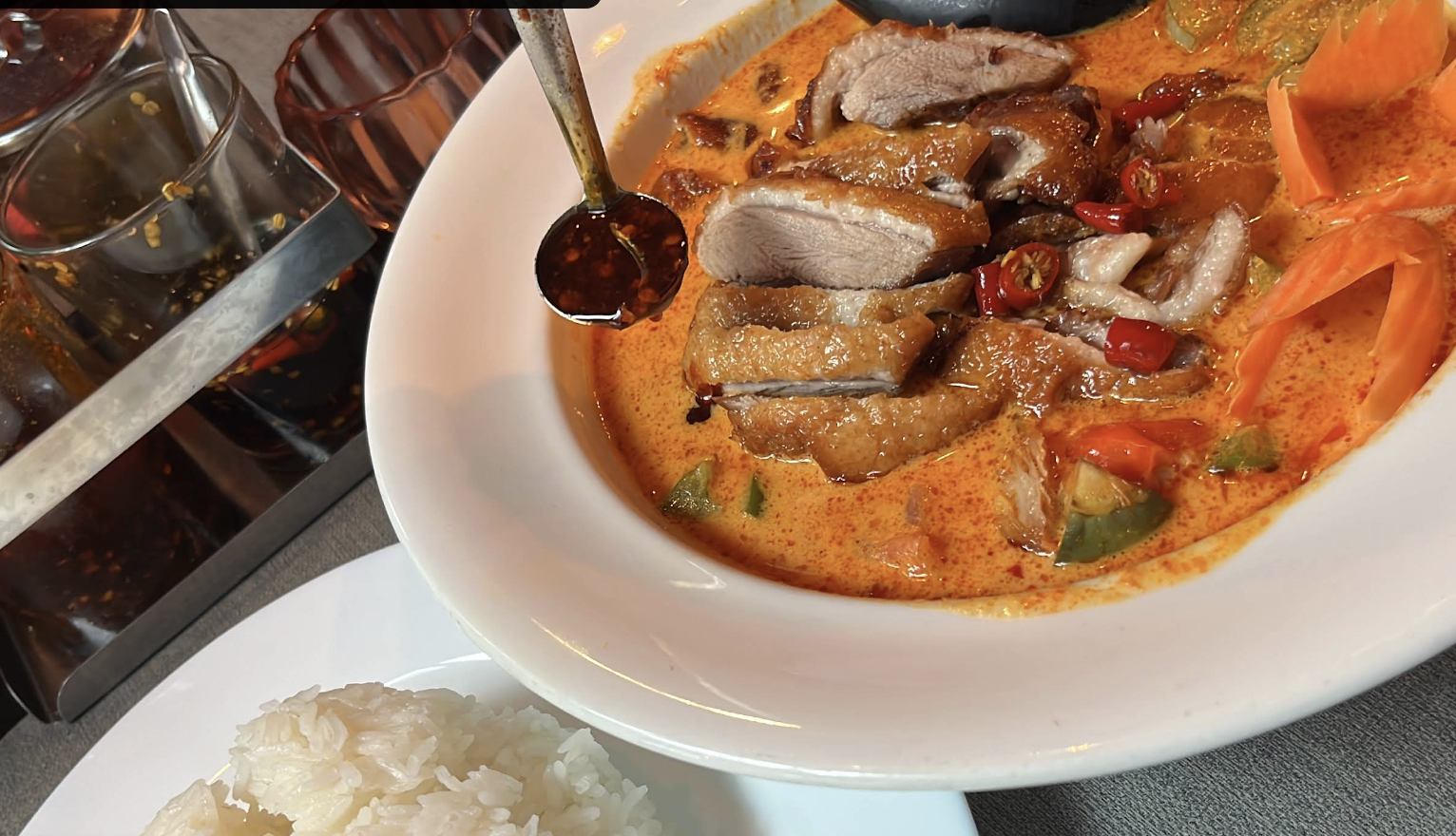 Rotes Curry des Capsule Hotels mit gebratener Ente, Chilis und Gemüse, serviert mit gedämpftem Reis und Chiliöl.