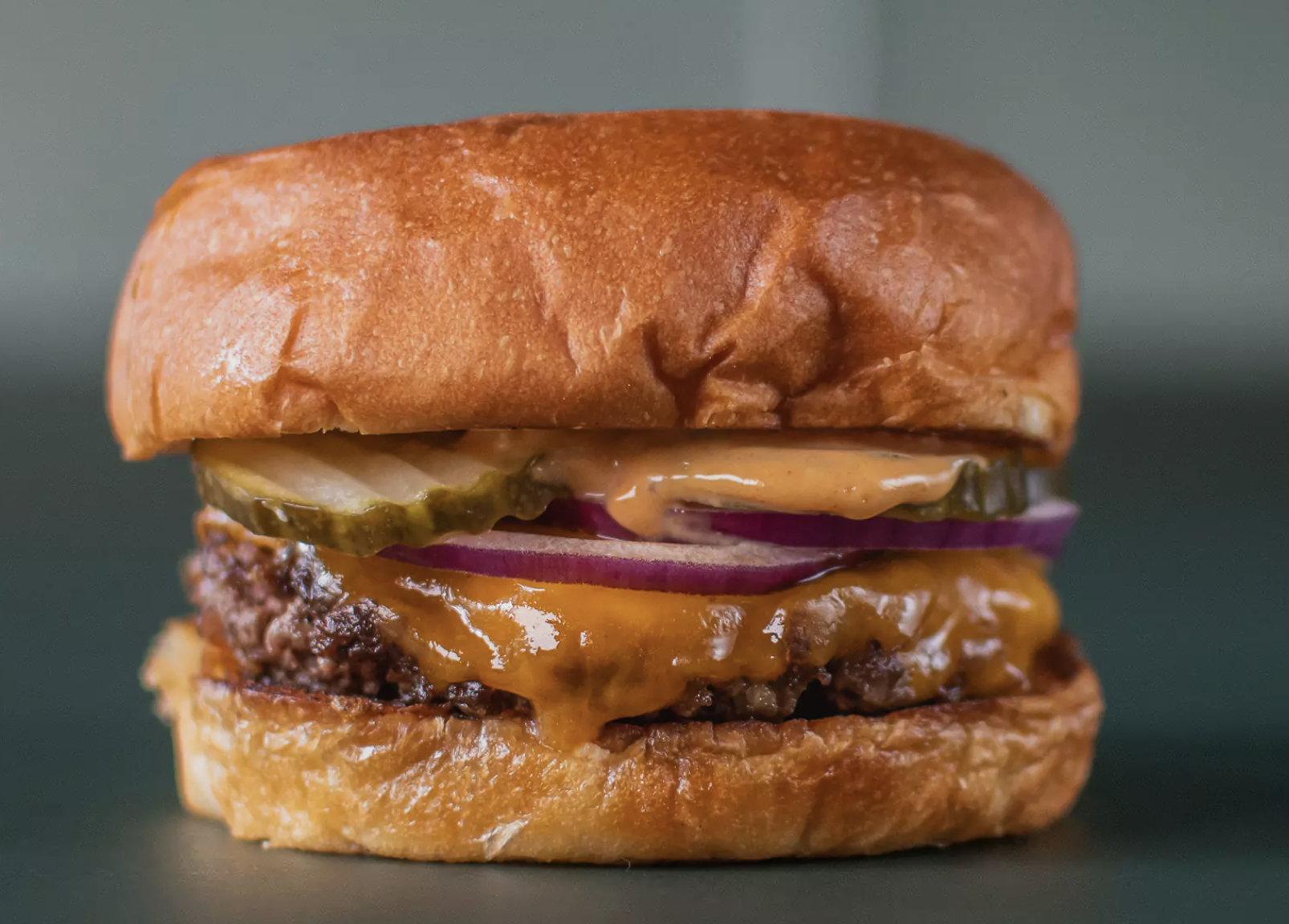 Gourmet-Cheeseburger im Capsule Hotel mit geschmolzenem Cheddar, Essiggurken, roten Zwiebeln und Sauce auf einem getoasteten Brioche-Brötchen.