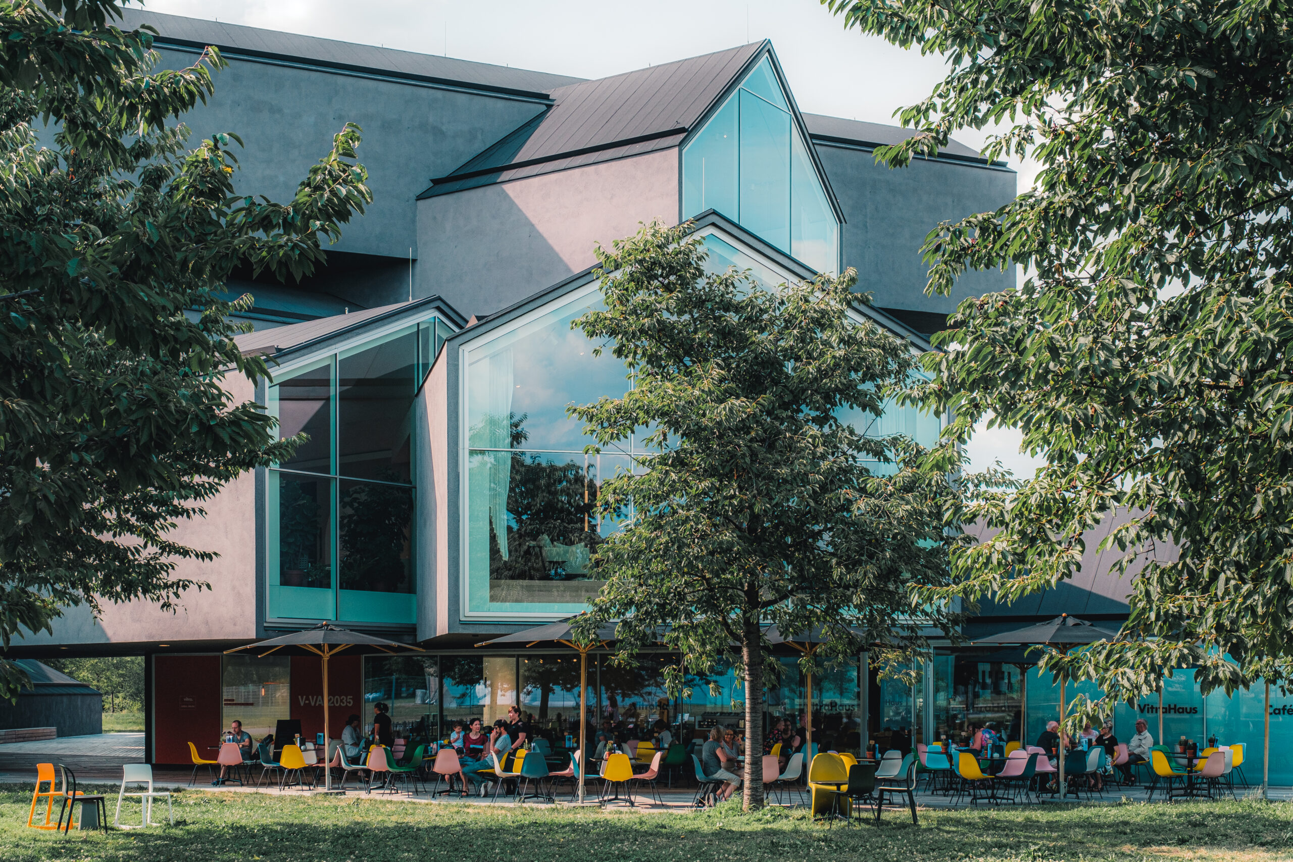 Das VitraHaus mit gestapelten Glasfassaden mit Giebel und einer Caféterrasse mit bunten Stühlen, Weil am Rhein