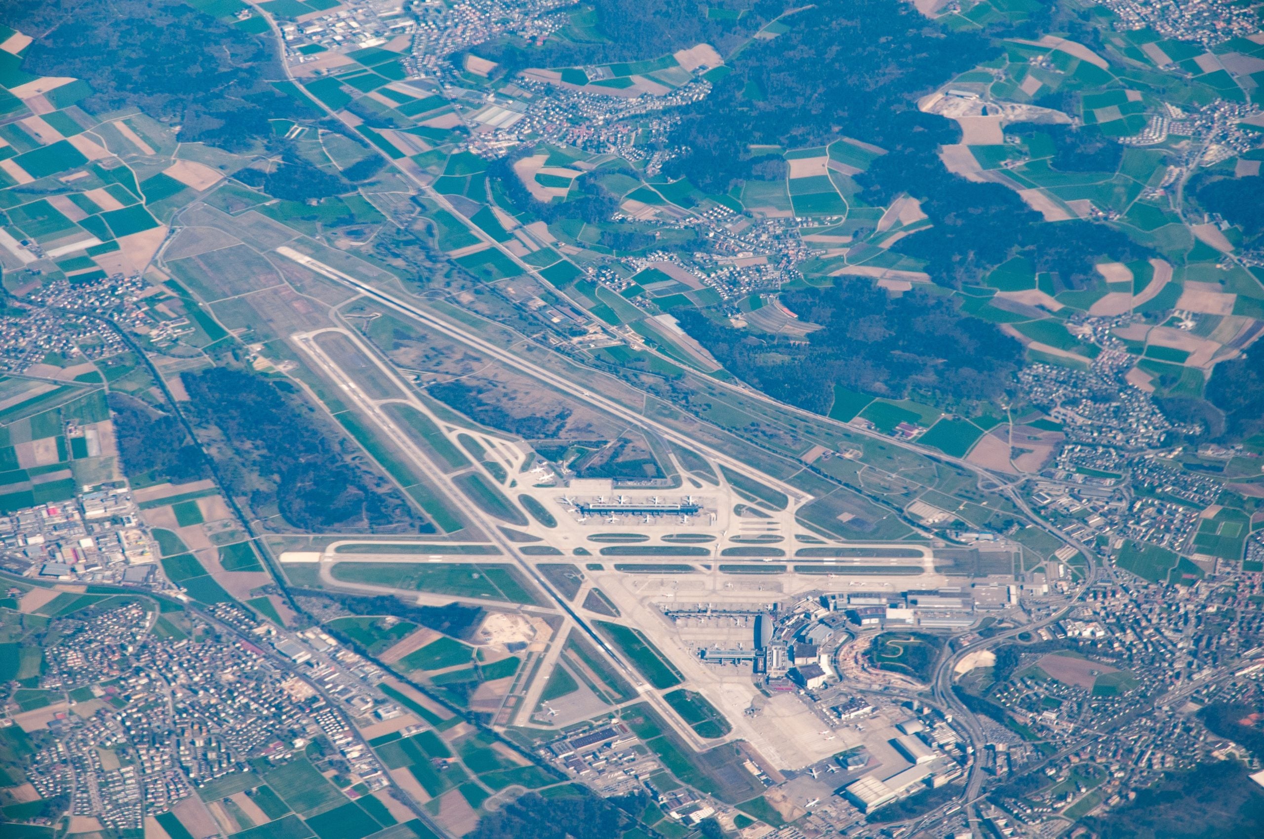 Aerial view of Zurich Airport, location of Capsule Hotel Alpine Garden Zurich Airport, surrounded by fields and town.