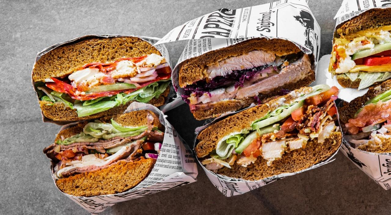 Verschiedene Gourmet-Sandwiches mit frischen Füllungen auf dunklem Brot, in Papier eingewickelt, im Capsule Hotel.