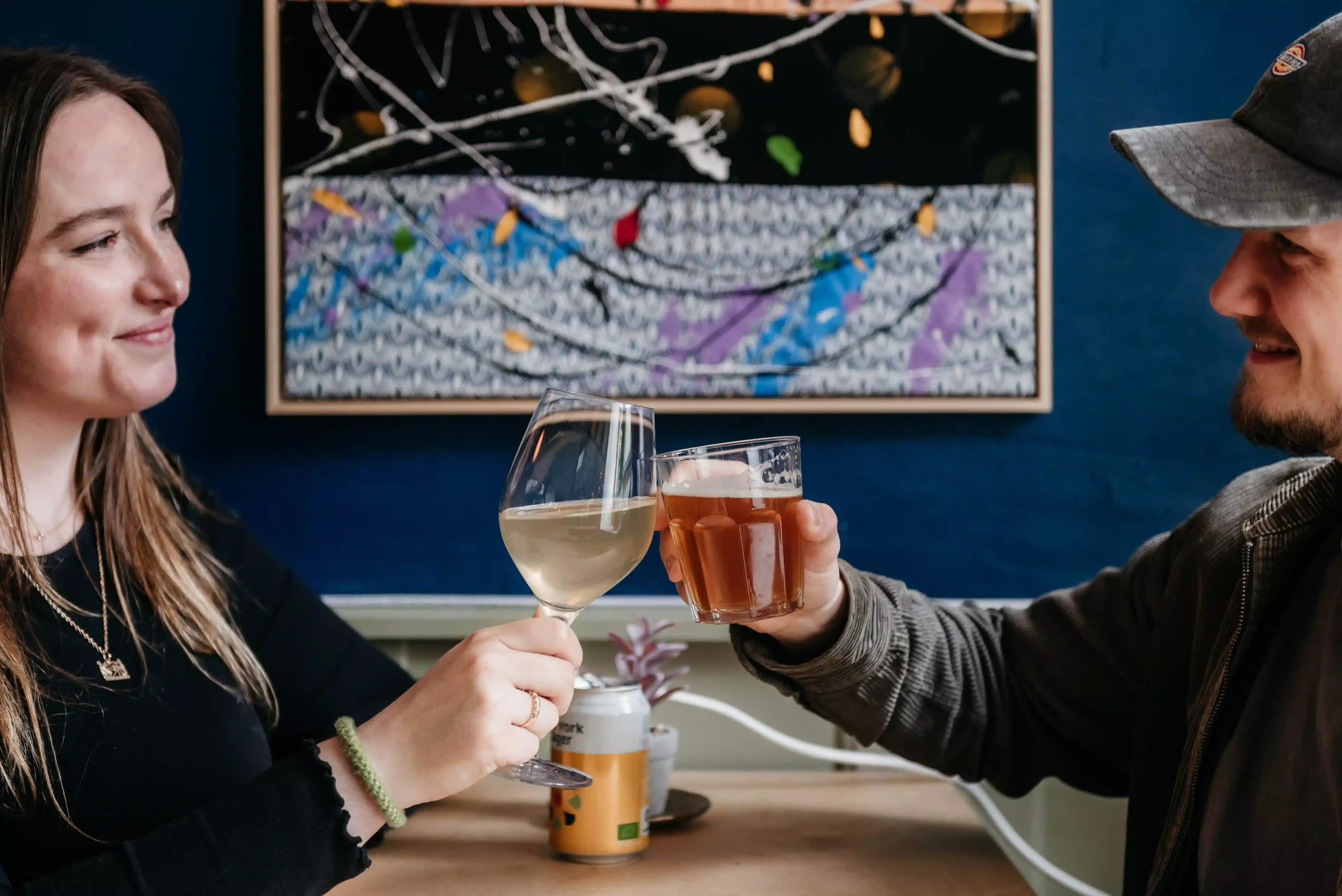 Cheers with wine and beer in the lounge at Capsule Hotel Copenhagen Vesterbro, with colorful artwork in the background.