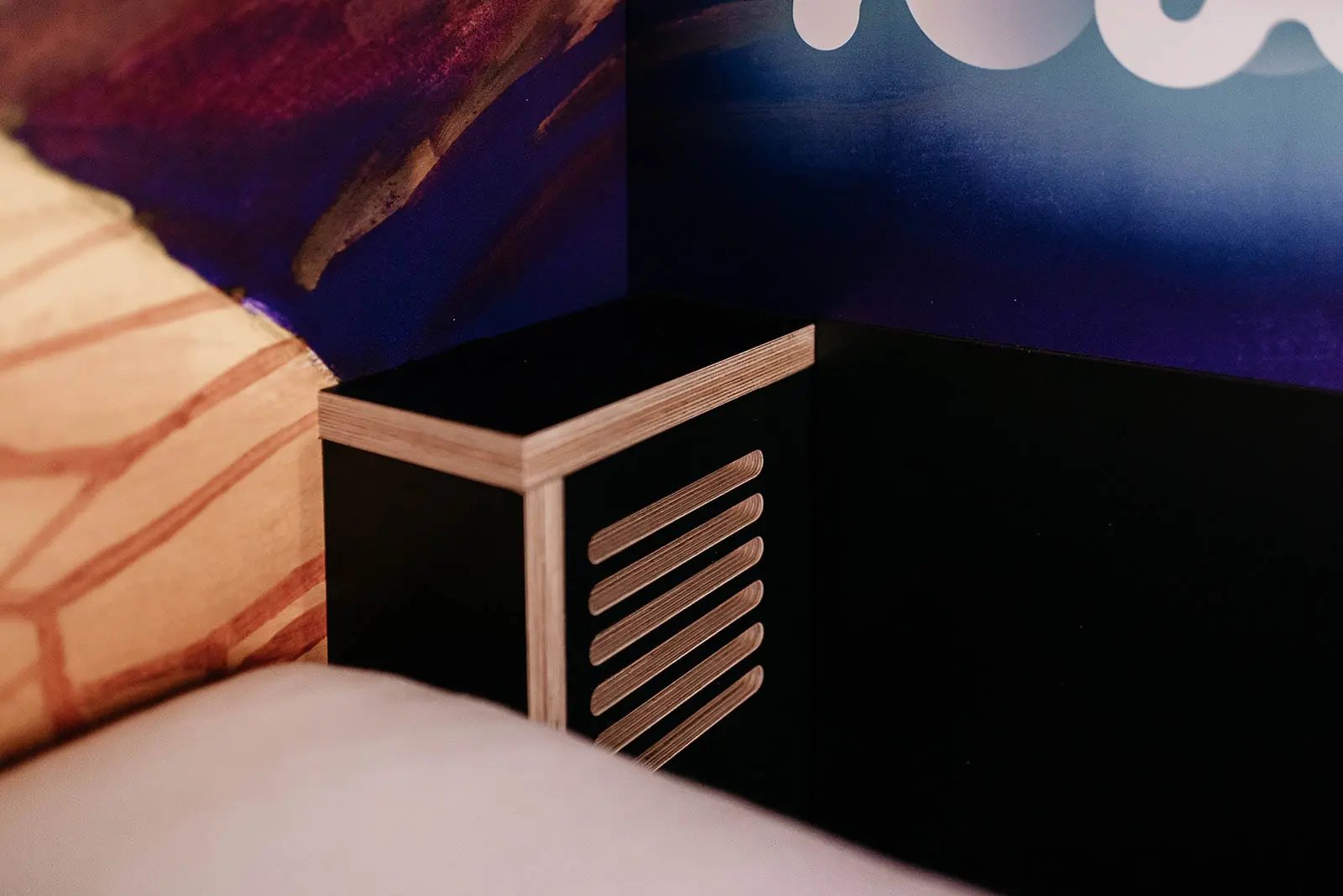 Wooden bedside shelf in a cozy capsule room at Capsule Hotel Lucerne Old Town, featuring modern design and vibrant wall art.