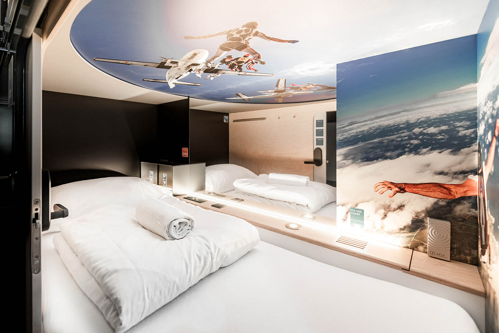 Spacious capsule room with aviation-themed ceiling artwork at Capsule Hotel Lucerne The Lab.