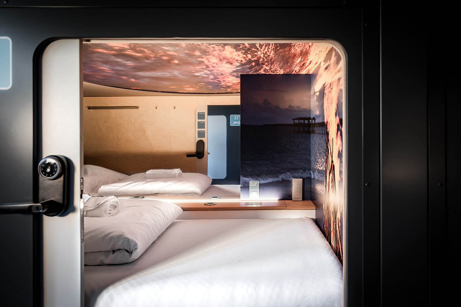 Cozy capsule room with scenic wall art and ambient lighting at Capsule Hotel Lucerne The Lab, featuring a comfortable bed.