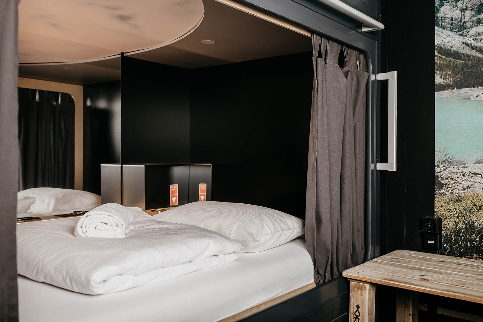Capsule room interior with cozy bed and rolled towel at Capsule Hotel Alpine Garden Zurich Airport.
