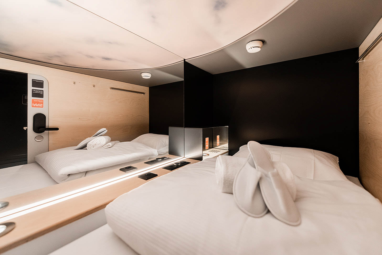 Capsule room interior with cozy bed, slippers, and ambient lighting at Capsule Hotel Alpine Garden Zurich Airport.