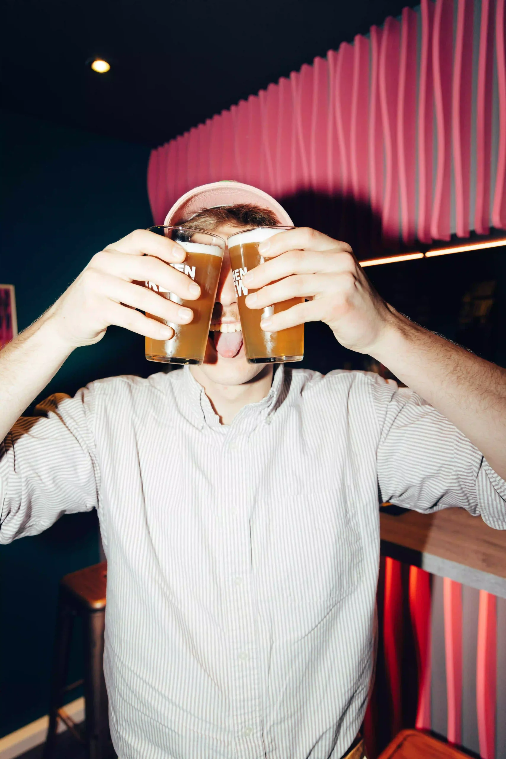 Man holding two beer glasses, playfully posing at Hyve Basel Capsule Hotel's vibrant bar area.