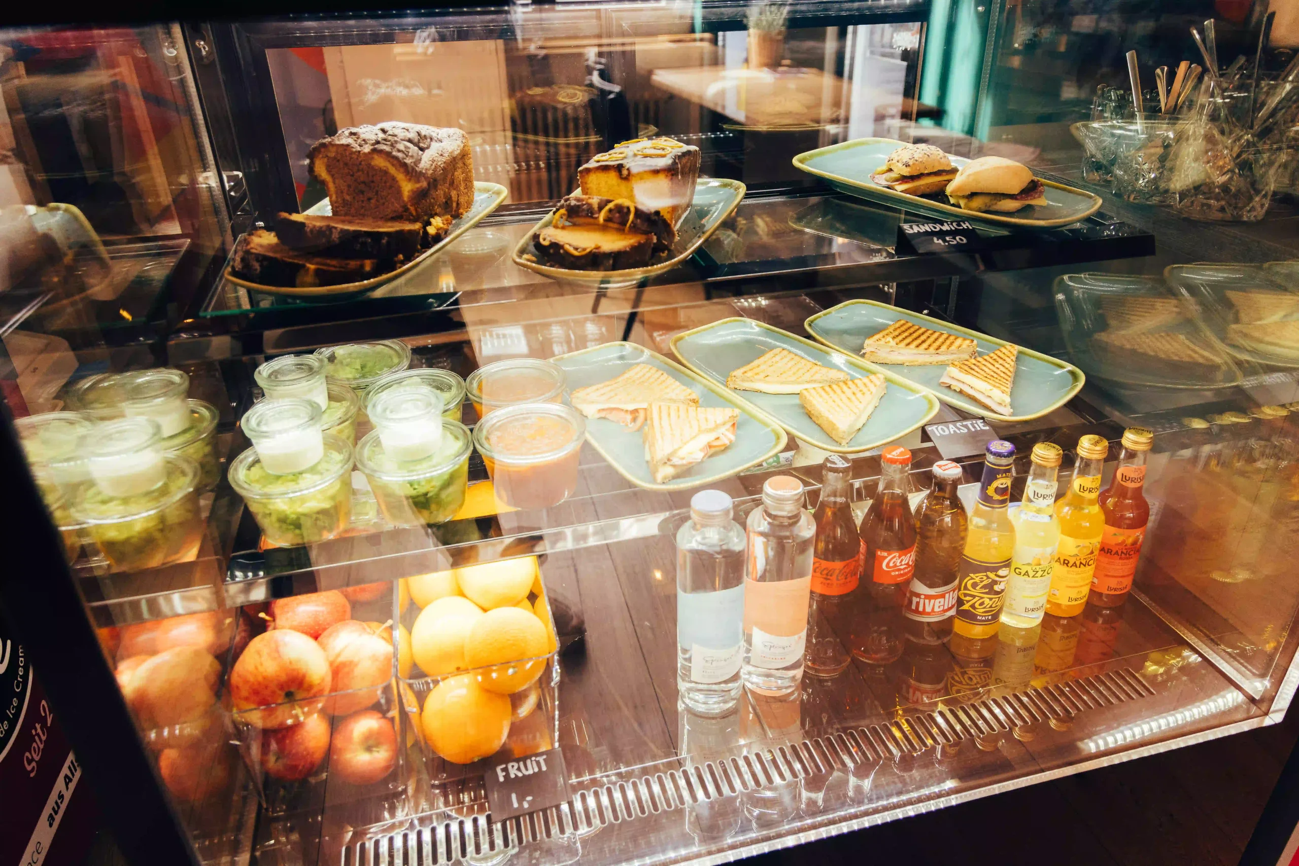 Beverage and snack display with sandwiches, toasties, and drinks at Hyve Basel Capsule Hotel.