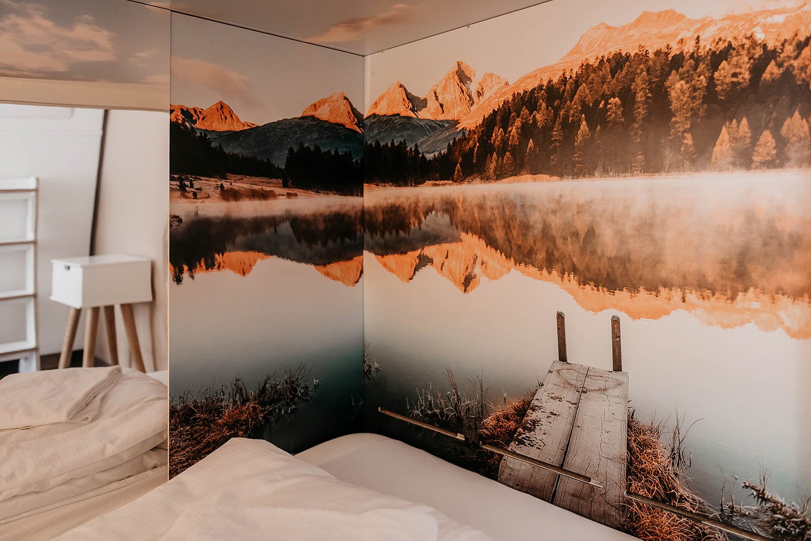 Mountain lake mural in a cozy capsule room at Hyve Basel Capsule Hotel, enhancing a tranquil atmosphere.