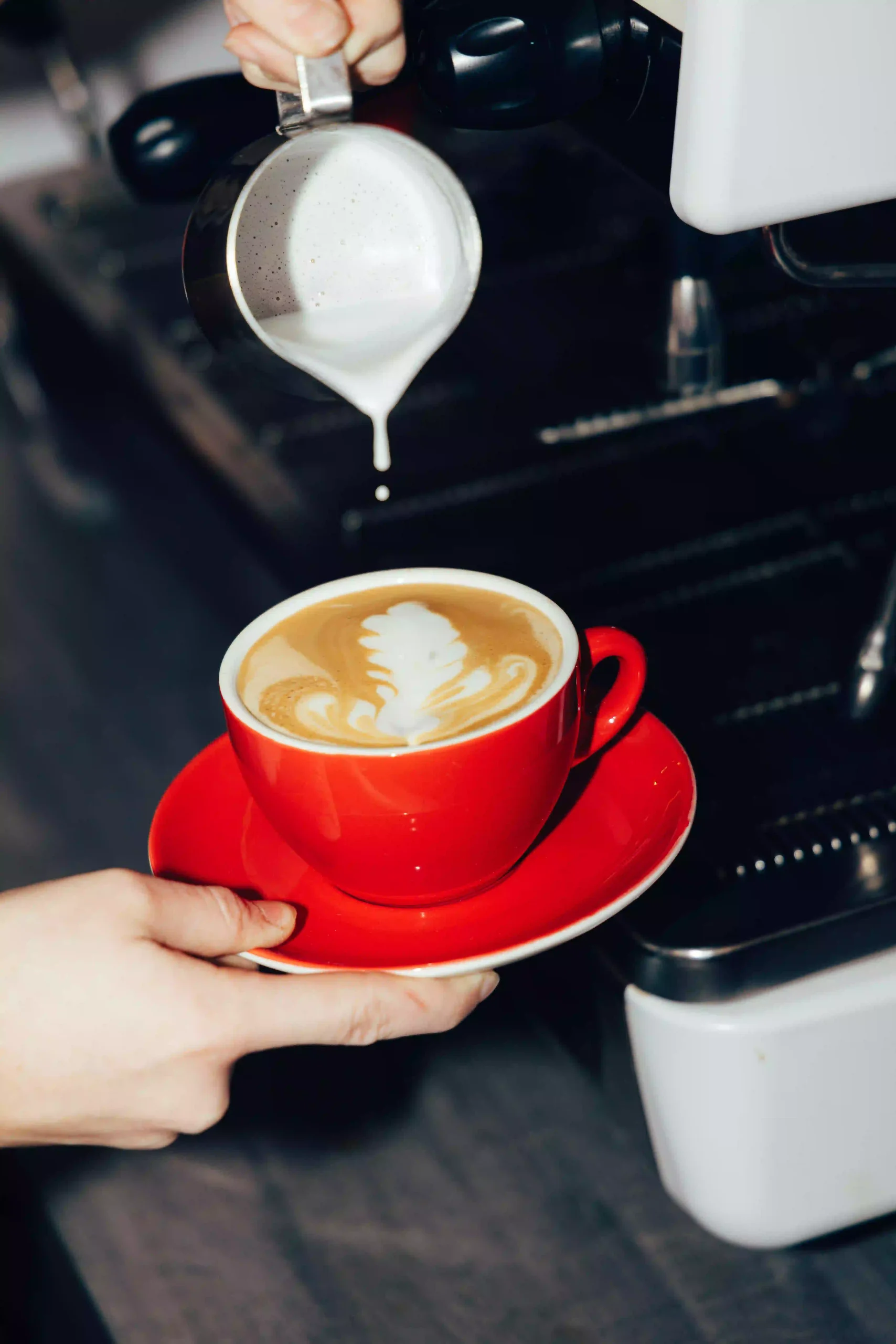 Latte art being crafted in a red cup at Hyve Basel Capsule Hotel cafe.