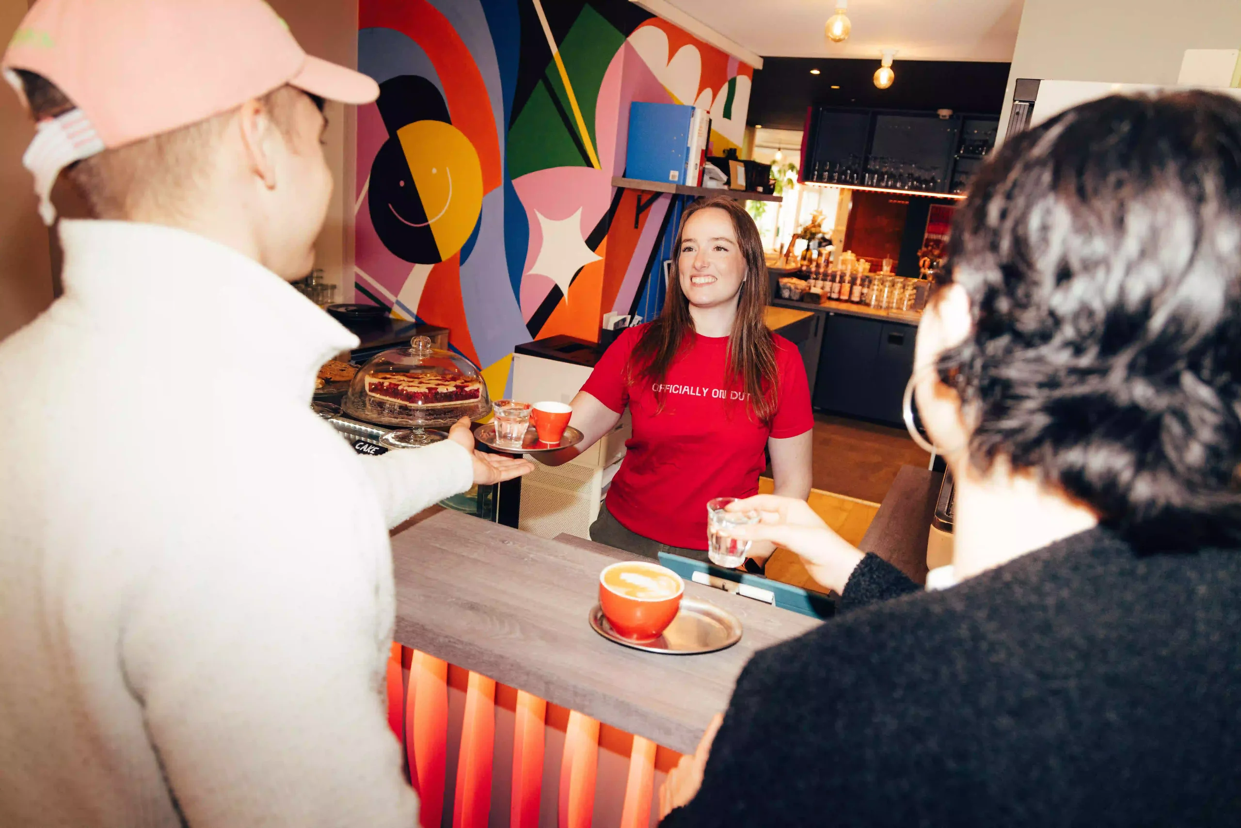 Bar area with colorful mural and staff serving drinks at Hyve Basel Capsule Hotel.