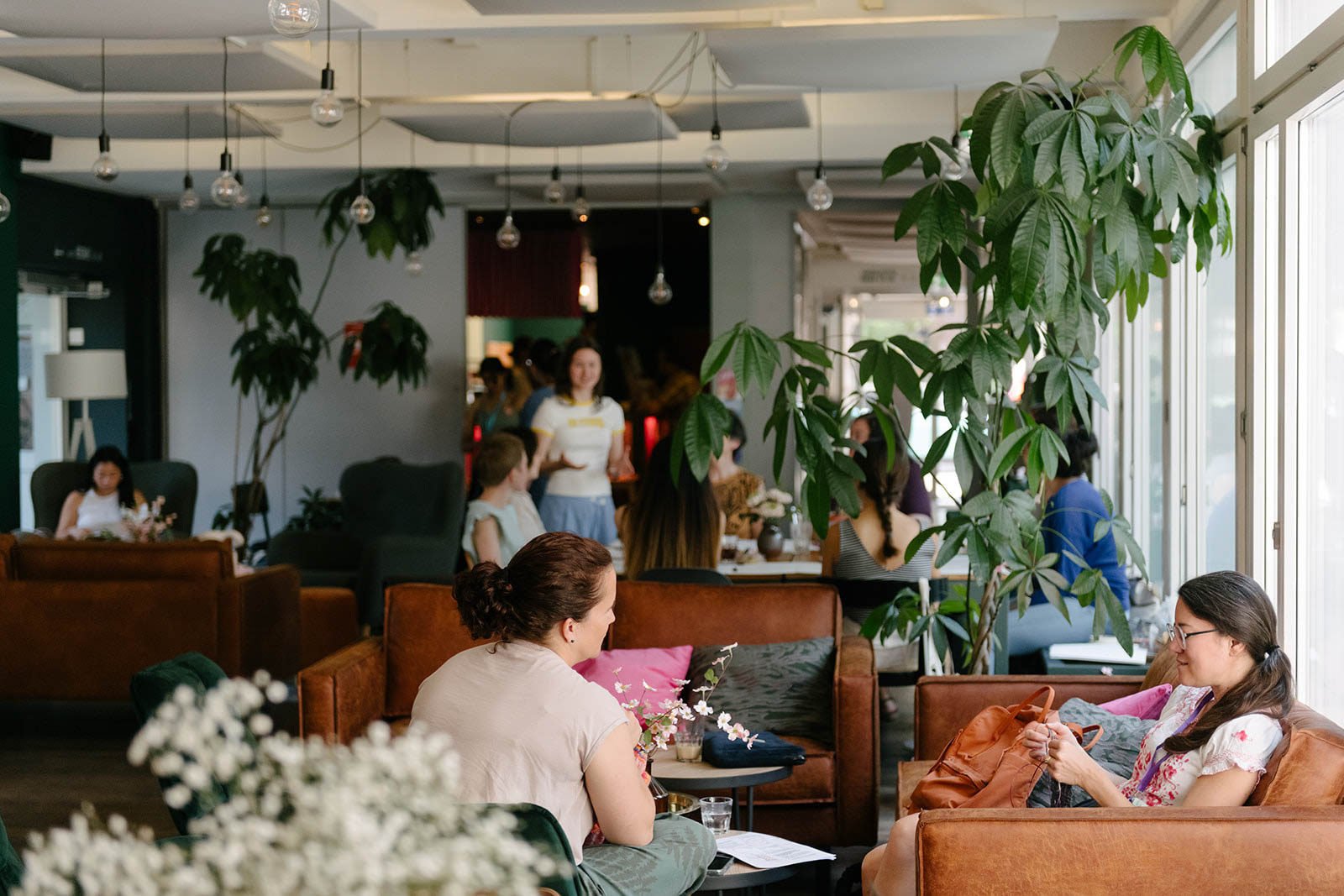 Cozy lounge area with guests relaxing at Hyve Basel Capsule Hotel, featuring modern decor and lush greenery.