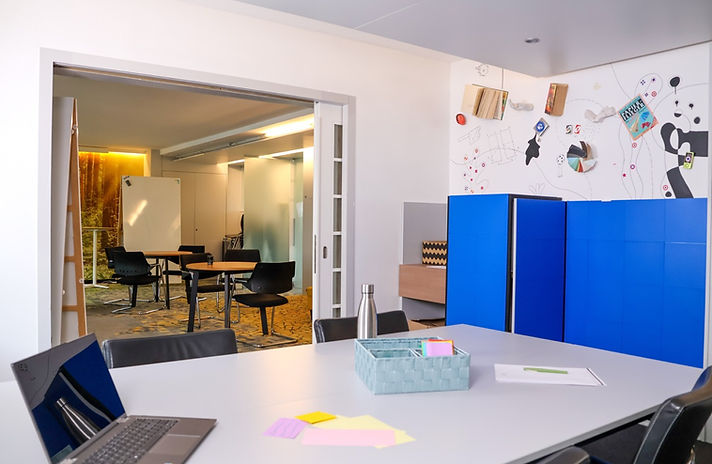 Capsule Hotel creative workspace with meeting table, blue lockers, wall art, and open doors to lounge spaces