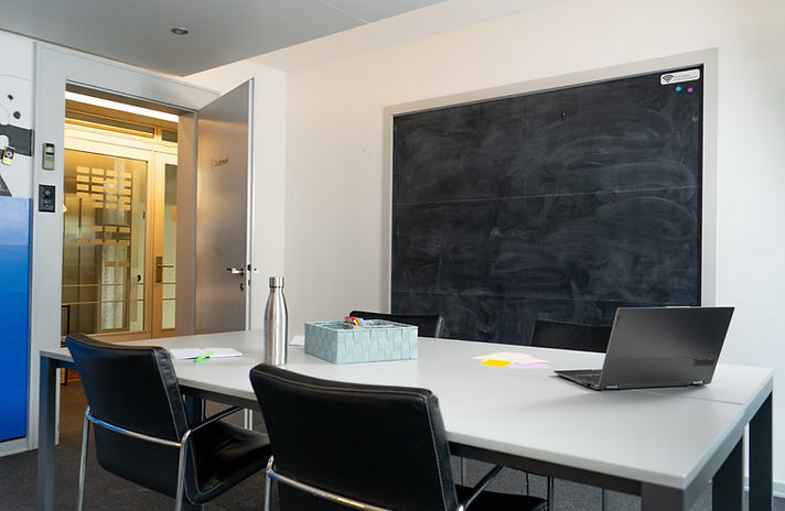 Meeting room at Capsule Hotel with modern furnishings, a large blackboard, and sleek seating for collaboration.