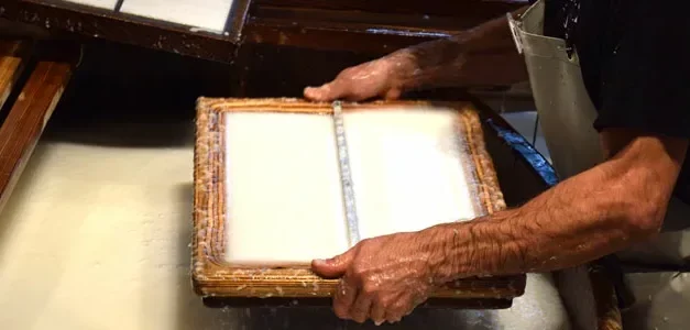 Die Hände eines Papiermachers heben in der Basler Papierfabrik eine Holzform mit zwei frischen Papierbögen an