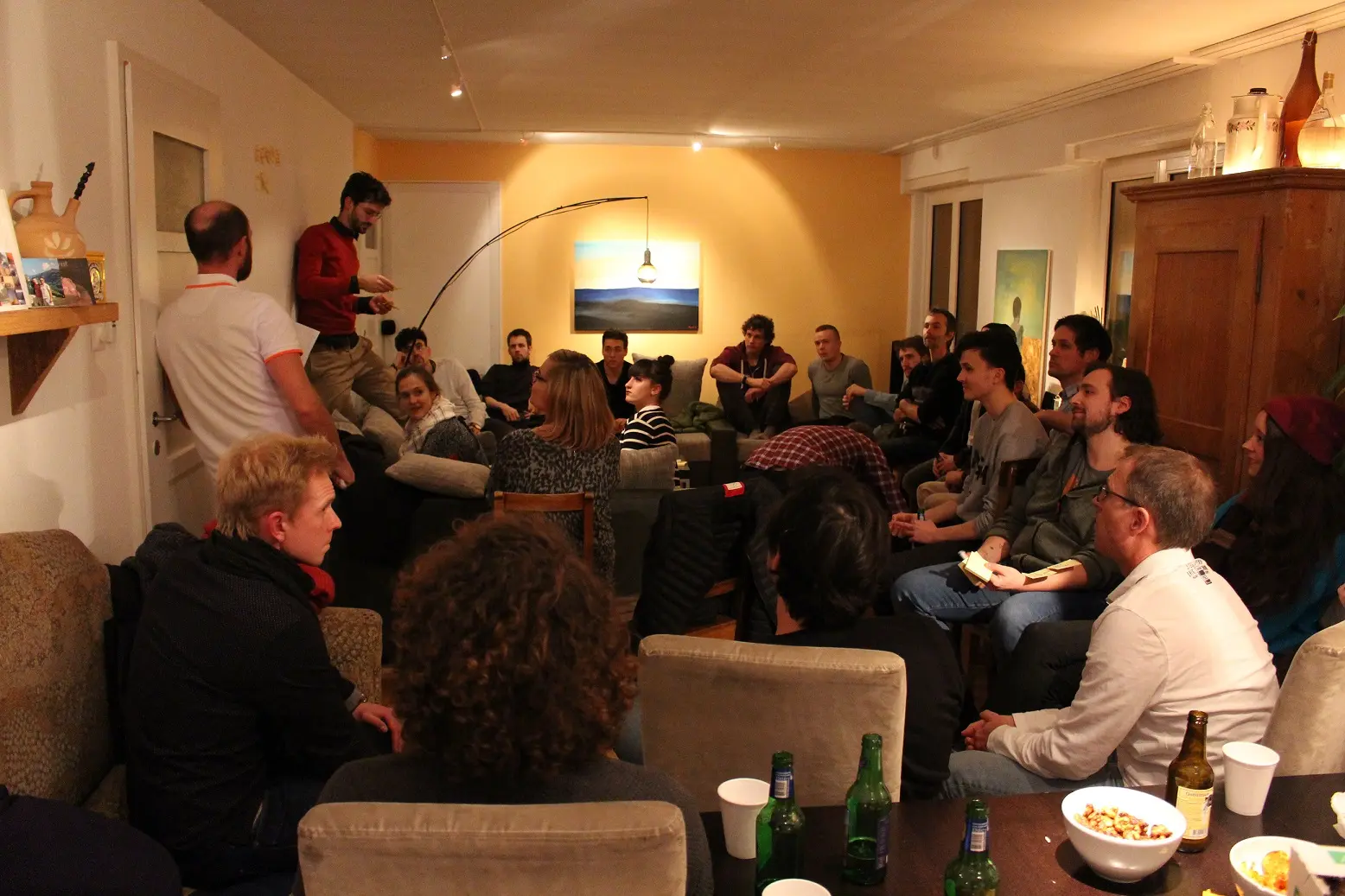 Group of people socializing in a cozy common area at Capsule Hotel. Warm lighting creates an inviting atmosphere.