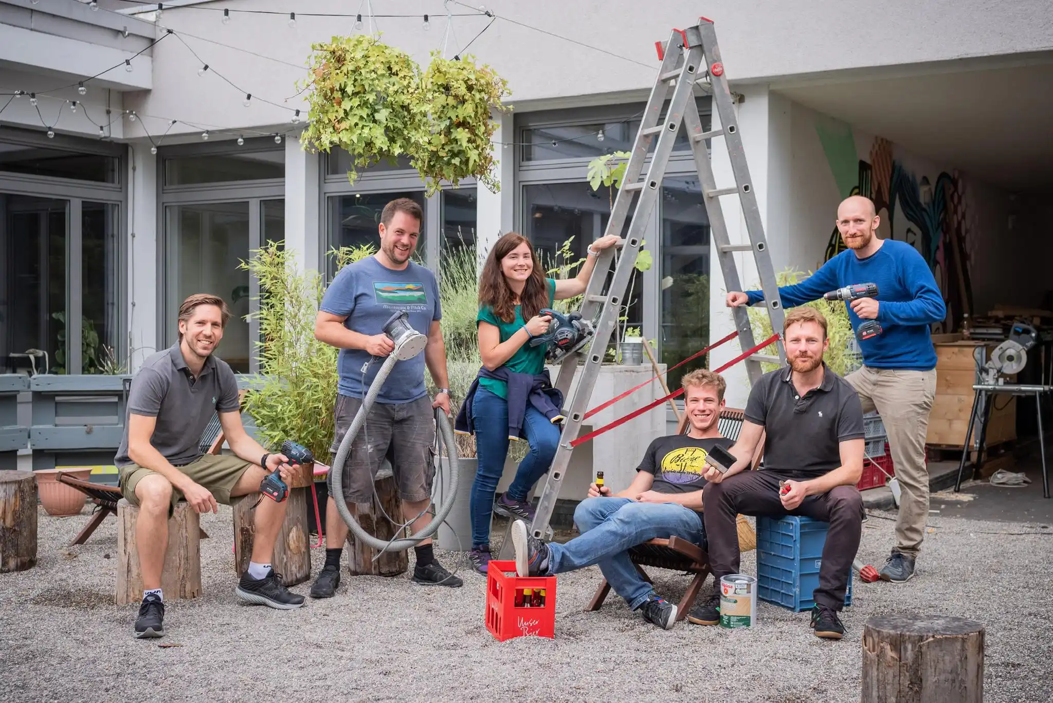 Team collaborating with tools at a Capsule Hotel outdoor space. Relaxed atmosphere showcasing creativity and teamwork.