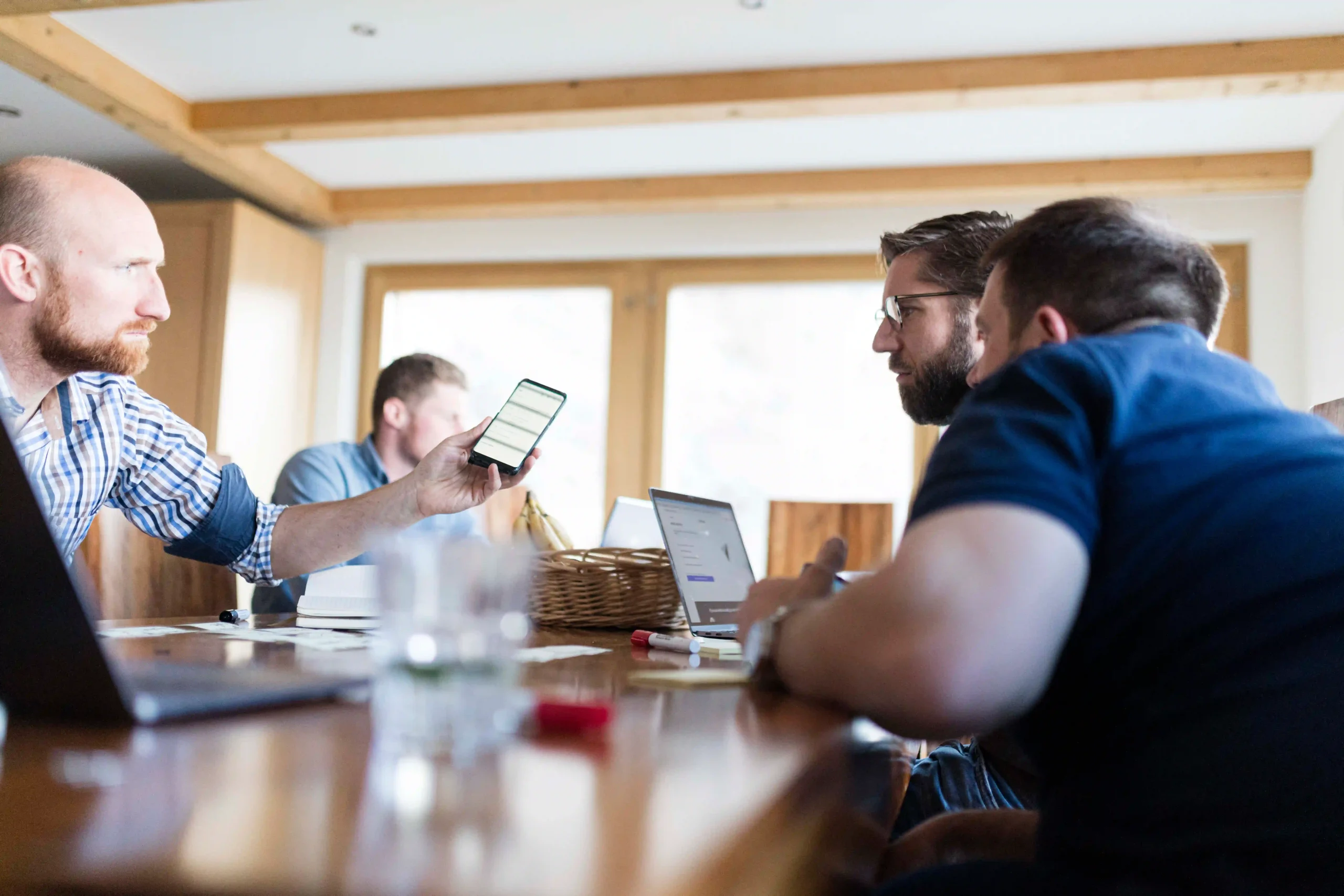 Team collaborating at a wooden table with laptops at Capsule Hotel, showcasing dynamic and productive environment.