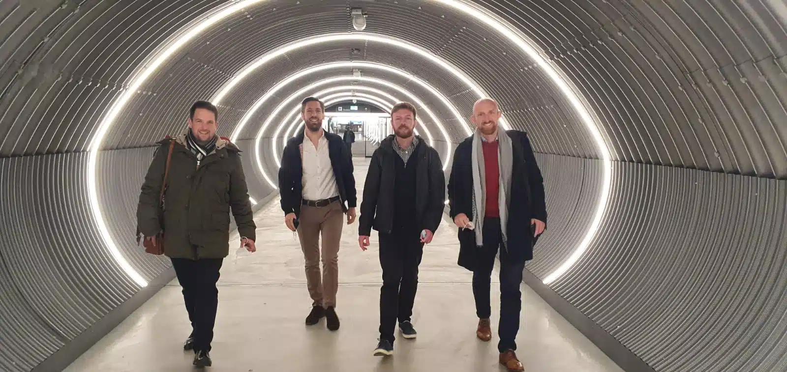 Four Capsule Hotel team members walking confidently through a futuristic, illuminated tunnel in European location.