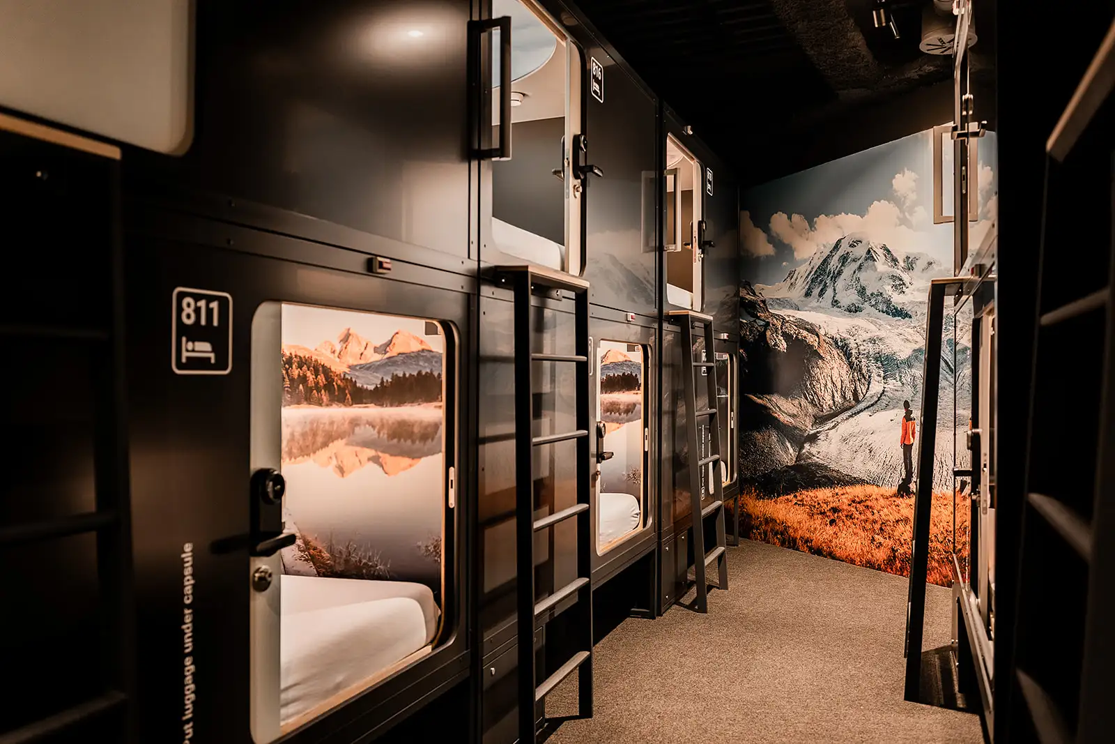 Modern sleeping pods in Capsule Hotel with nature-themed wall art. Cozy and minimalist design in a shared area.