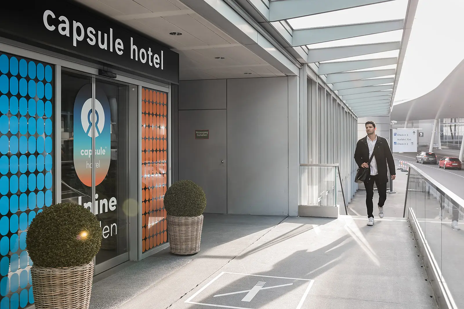 Capsule Hotel entrance with modern signage and a man walking by, showcasing sleek, urban design elements.