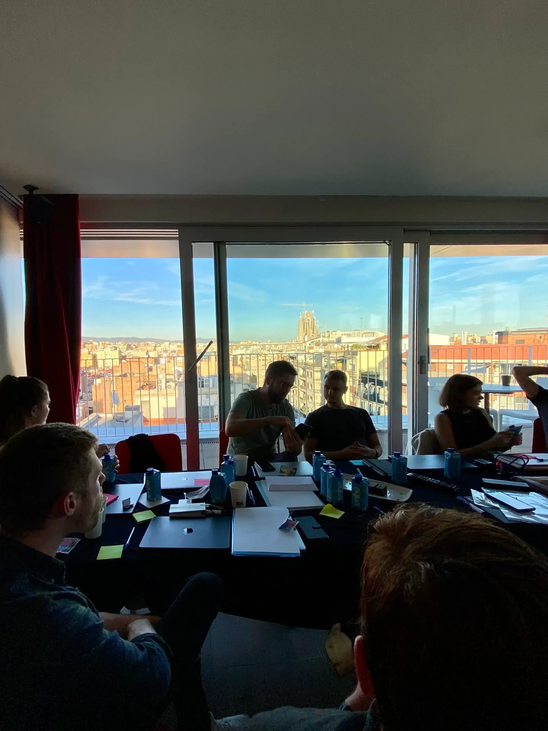 Team meeting in a bright room with a cityscape balcony view at Capsule Hotel, showcasing collaboration and creativity.