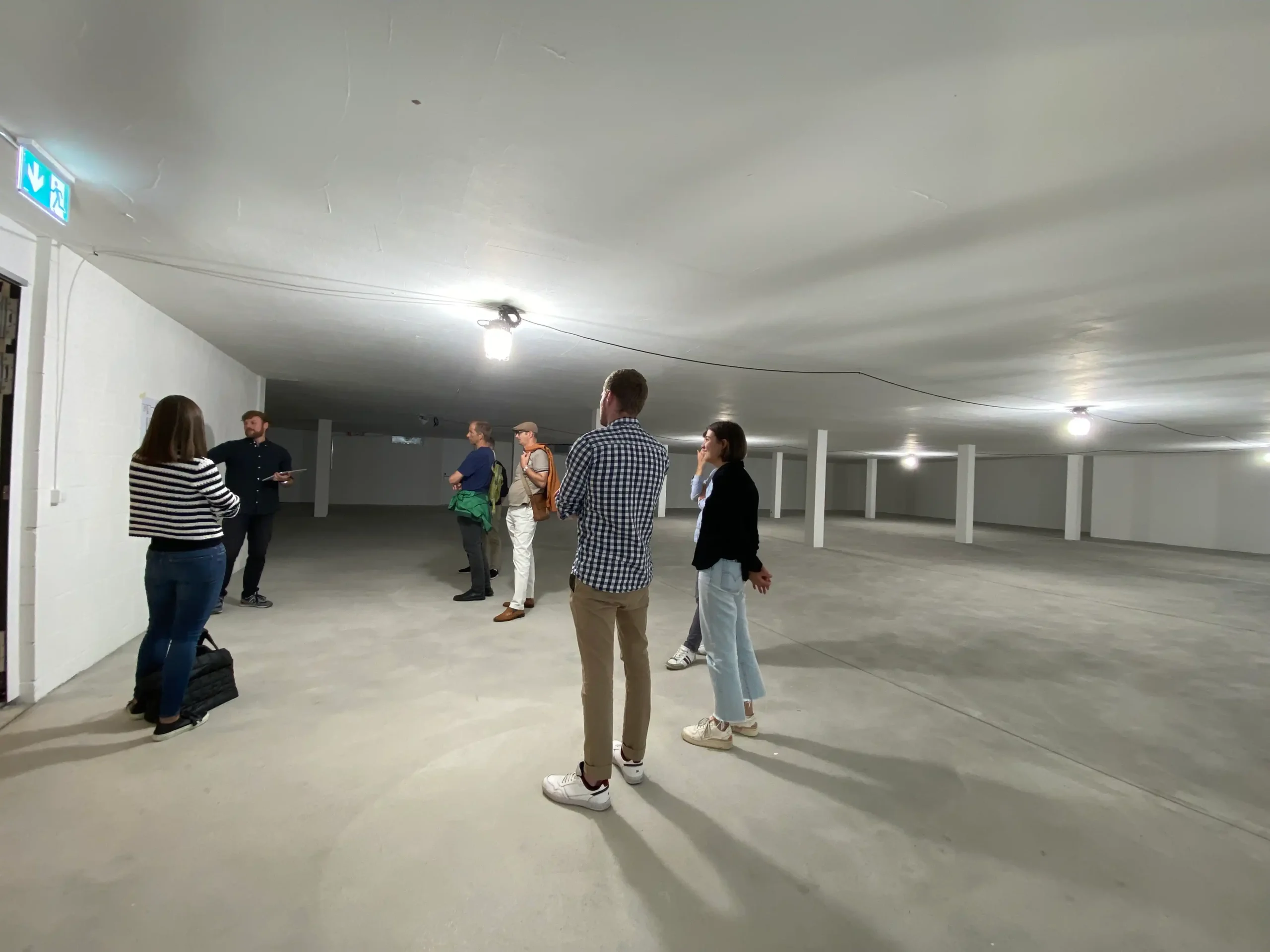 Capsule Hotel team in a spacious, well-lit, unfinished area discussing plans. Casual attire and engaged conversation.