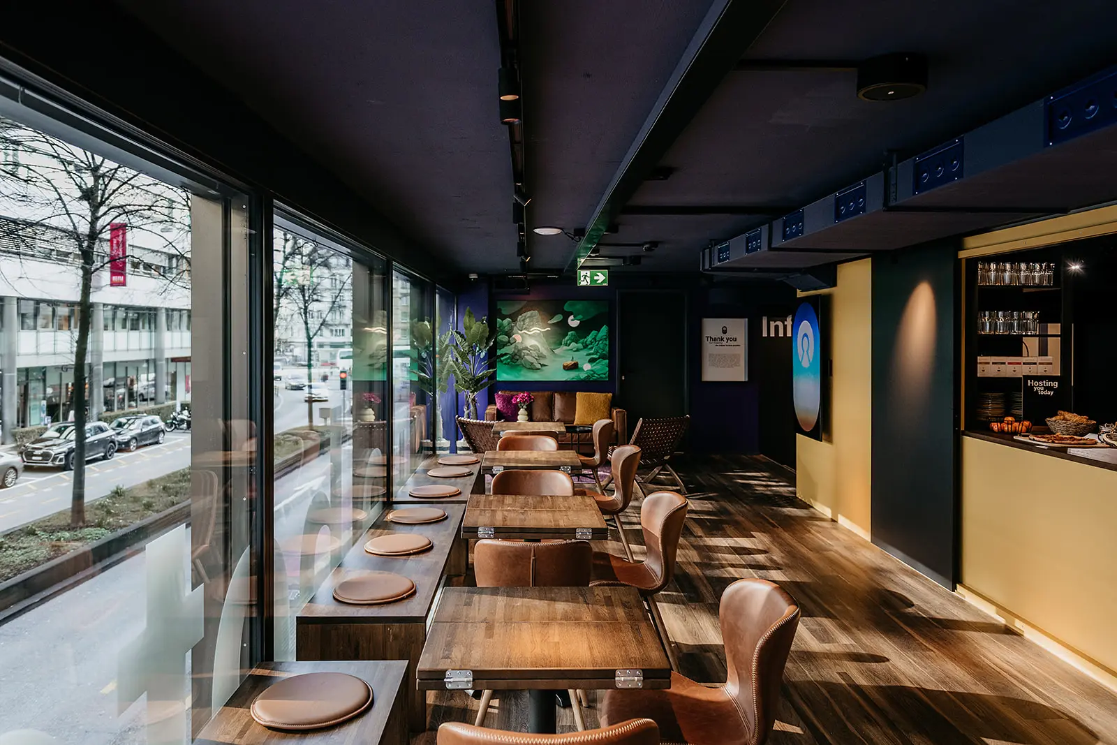 Modern Capsule Hotel dining area with wooden tables, leather chairs, large windows, and cozy decor.