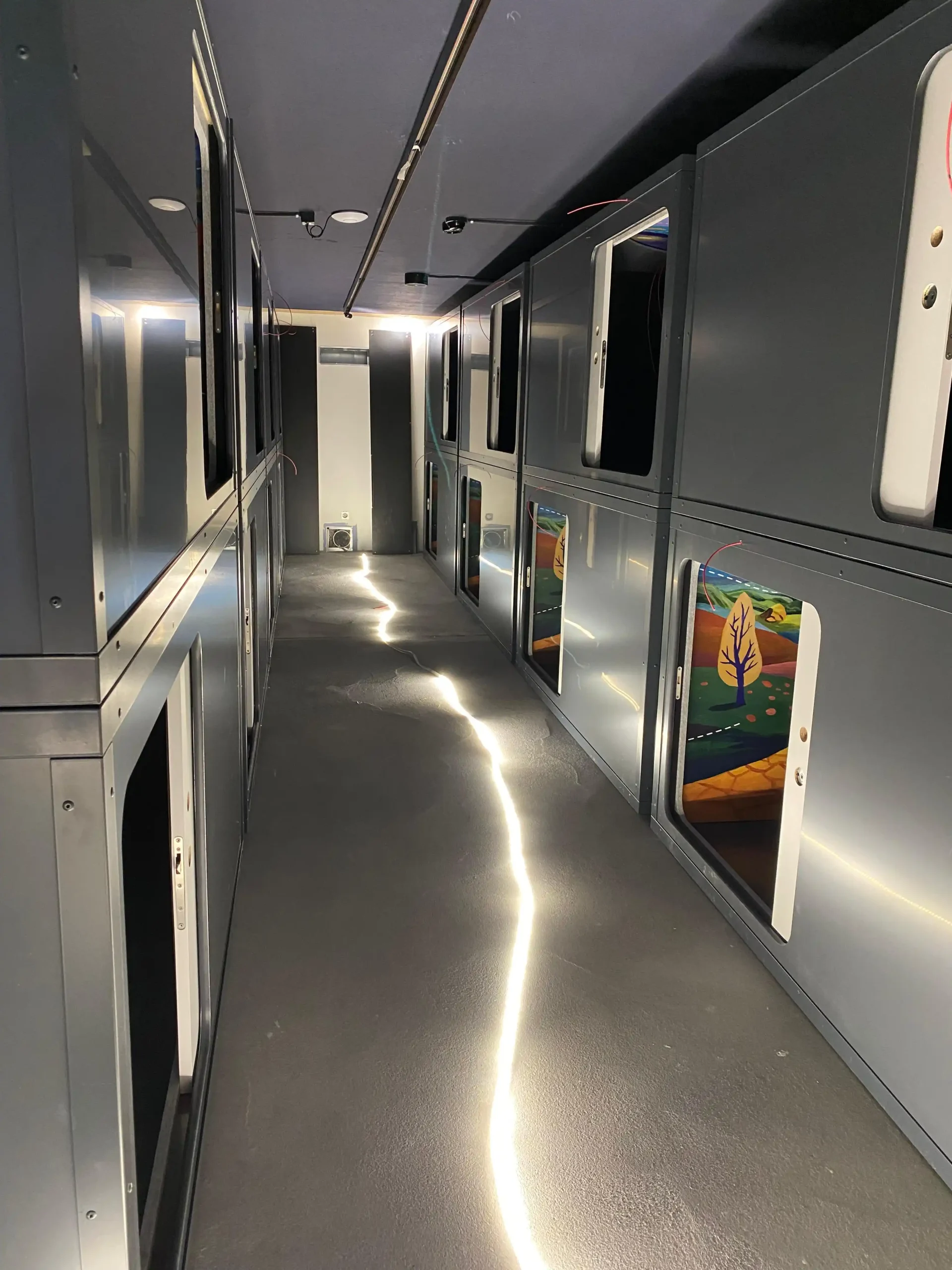 Modern hallway with sleek, illuminated sleeping pods at Capsule Hotel, reflecting contemporary design and comfort.