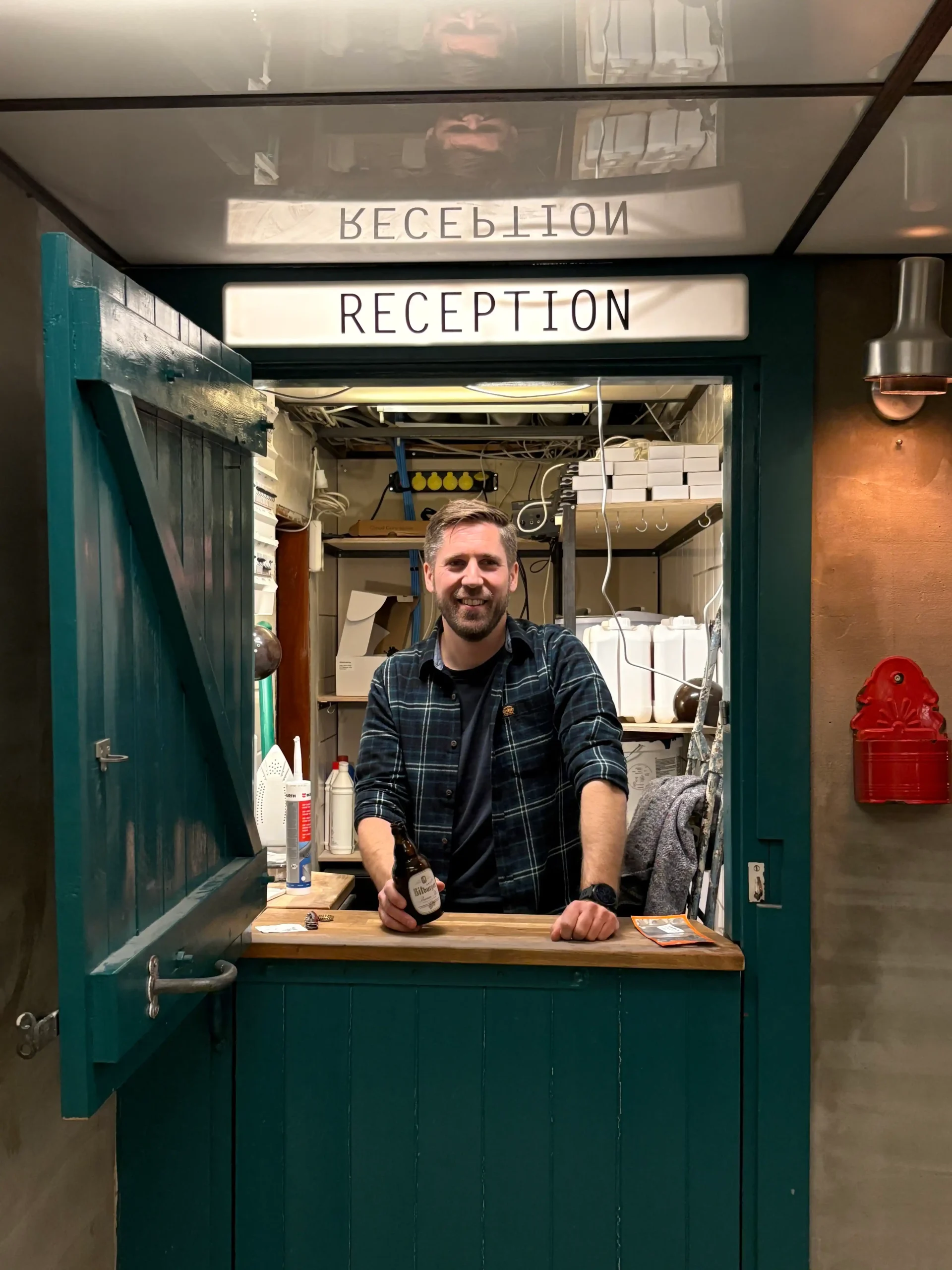 Team member welcoming guests at Capsule Hotel reception, holding a bottle. Cozy hospitality in a stylish setting.